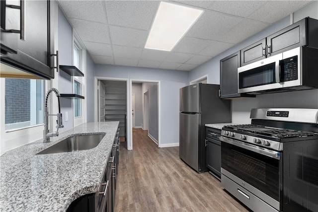 kitchen with light stone countertops, light wood-style flooring, a drop ceiling, a sink, and appliances with stainless steel finishes