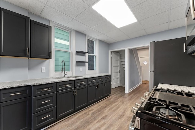 kitchen featuring light wood-type flooring, a sink, a drop ceiling, freestanding refrigerator, and range with gas cooktop