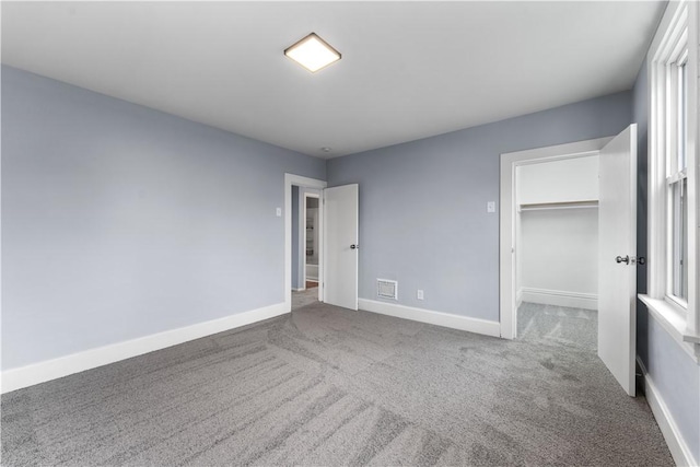 unfurnished bedroom with carpet, visible vents, baseboards, a spacious closet, and a closet