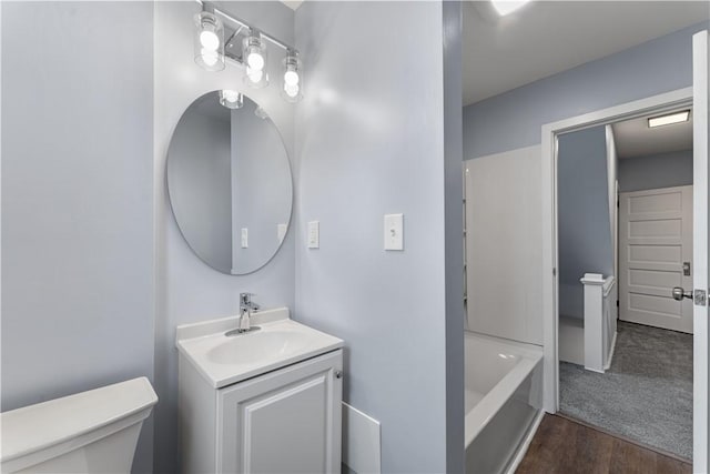 bathroom featuring a tub, toilet, wood finished floors, and vanity