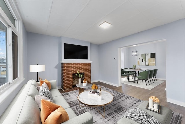 living room featuring a chandelier, a brick fireplace, baseboards, and wood finished floors