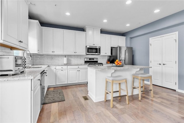 kitchen with light wood finished floors, a breakfast bar area, stainless steel appliances, white cabinetry, and a sink