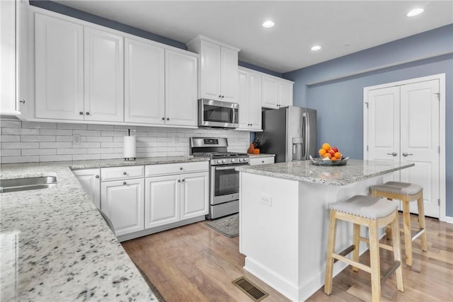 kitchen with a breakfast bar, white cabinets, appliances with stainless steel finishes, a center island, and light wood finished floors