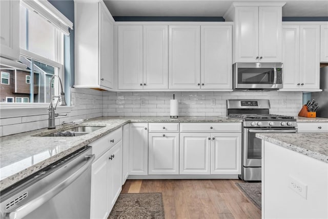 kitchen with backsplash, appliances with stainless steel finishes, white cabinetry, a sink, and light wood-type flooring