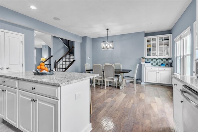 kitchen with white cabinetry, light wood-style floors, decorative backsplash, light stone countertops, and glass insert cabinets