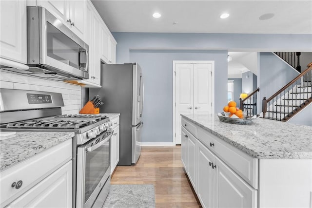 kitchen featuring stainless steel appliances, white cabinetry, light wood-style flooring, and decorative backsplash