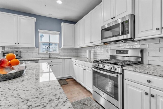 kitchen featuring decorative backsplash, white cabinets, appliances with stainless steel finishes, light stone countertops, and a sink