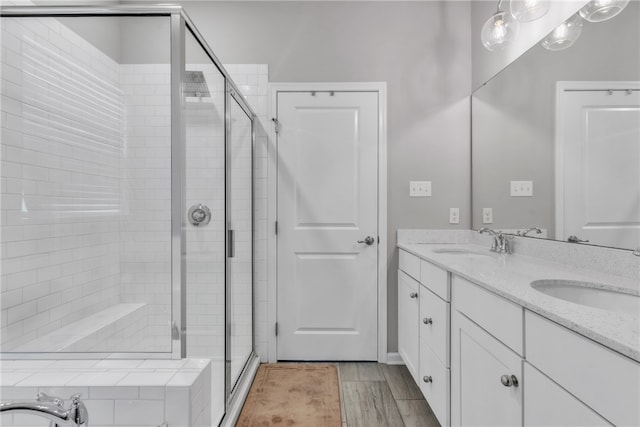 bathroom featuring double vanity, wood finished floors, a sink, and a shower stall