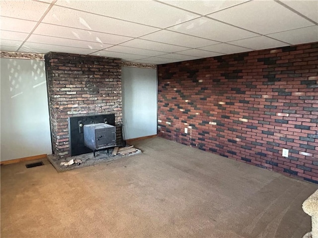 unfurnished living room with visible vents, a drop ceiling, brick wall, a wood stove, and carpet flooring