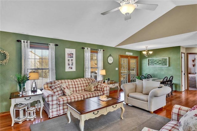 living room featuring vaulted ceiling, wood finished floors, and ceiling fan with notable chandelier