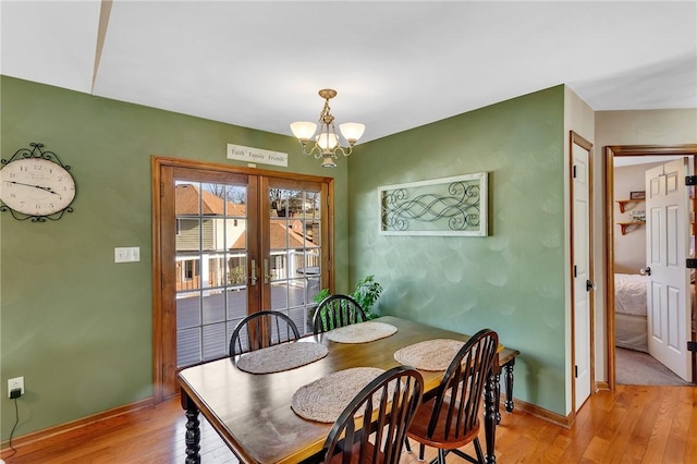 dining room featuring light wood-type flooring, french doors, a notable chandelier, and baseboards