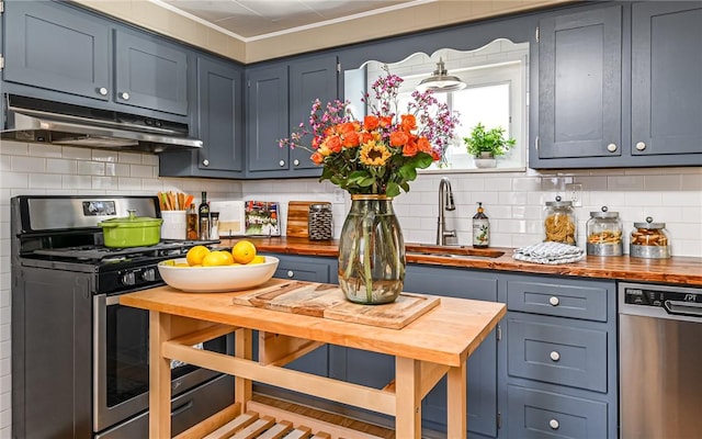 kitchen featuring tasteful backsplash, stainless steel appliances, under cabinet range hood, wooden counters, and a sink