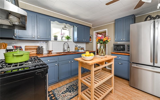 kitchen with wooden counters, appliances with stainless steel finishes, a sink, and blue cabinets