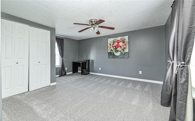 unfurnished bedroom with a closet, carpet flooring, ceiling fan, a textured ceiling, and baseboards