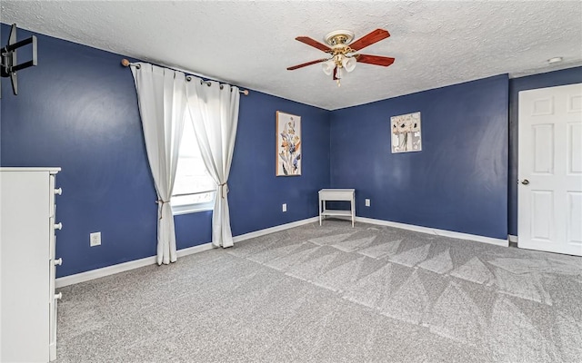 carpeted spare room featuring a textured ceiling, a ceiling fan, and baseboards