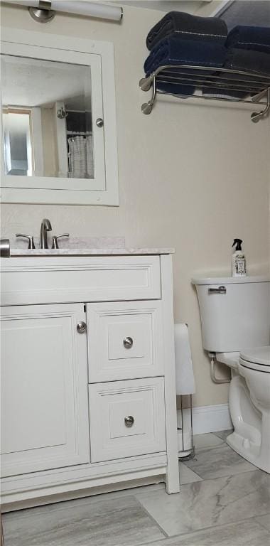 bathroom with toilet, marble finish floor, baseboards, and vanity