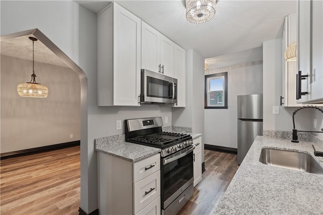 kitchen featuring appliances with stainless steel finishes, white cabinetry, a sink, wood finished floors, and a chandelier