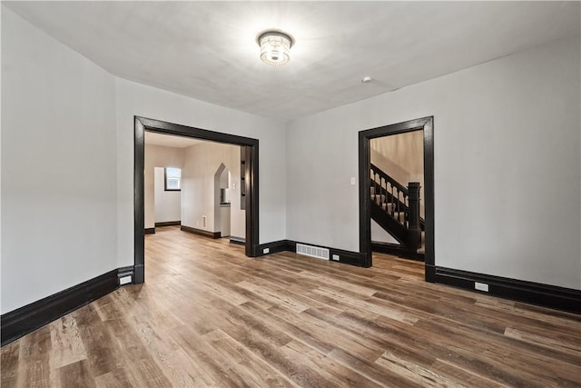 spare room featuring baseboards, visible vents, arched walkways, wood finished floors, and stairs