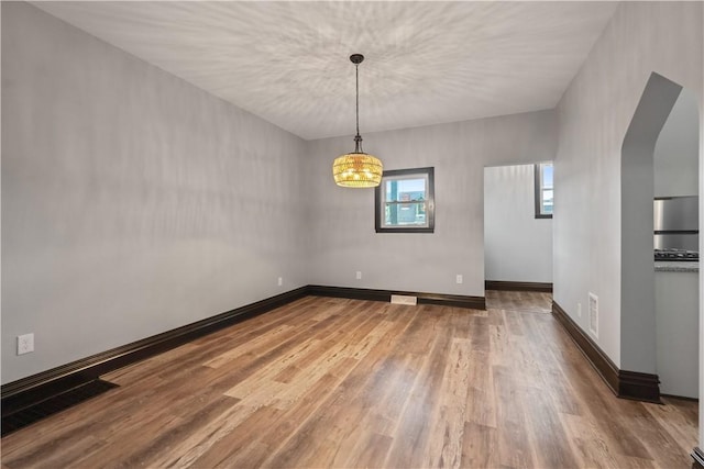 empty room featuring wood finished floors, visible vents, and baseboards