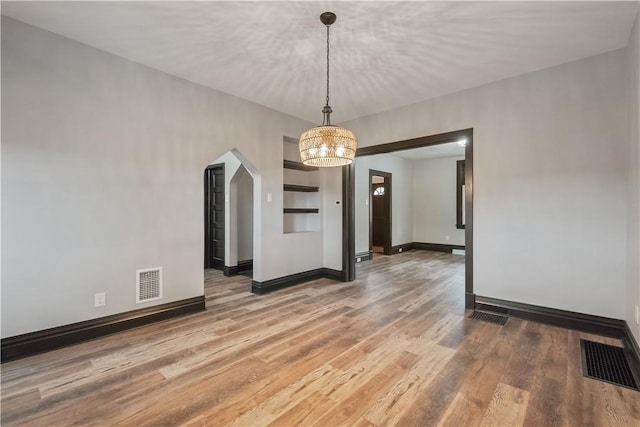 empty room featuring arched walkways, visible vents, baseboards, and wood finished floors