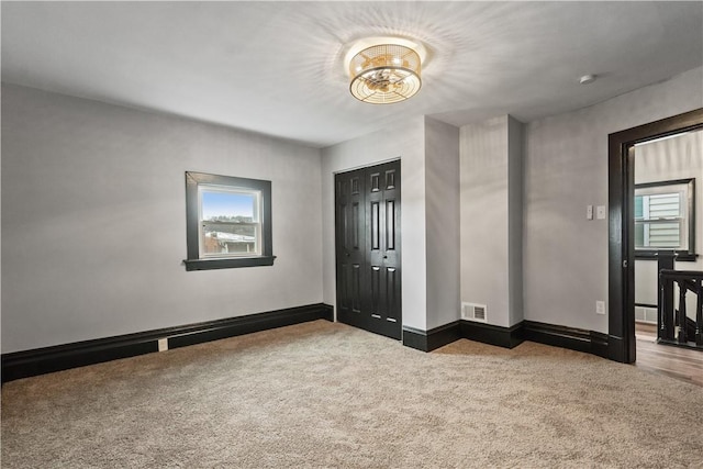 carpeted empty room with a chandelier, visible vents, and baseboards