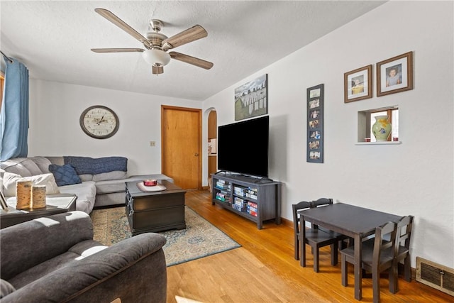 living area with arched walkways, light wood finished floors, visible vents, a ceiling fan, and baseboards