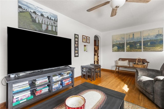 living room featuring baseboards, ceiling fan, arched walkways, and wood finished floors