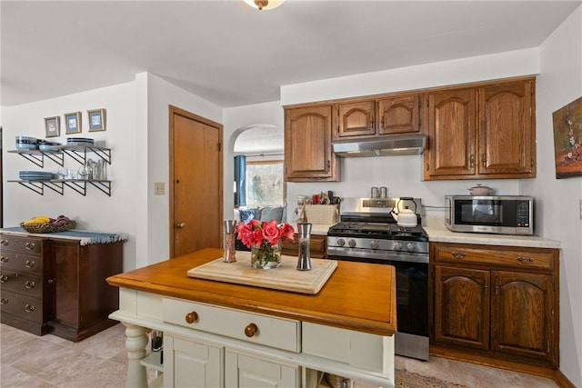 kitchen featuring arched walkways, brown cabinetry, stainless steel appliances, light countertops, and under cabinet range hood