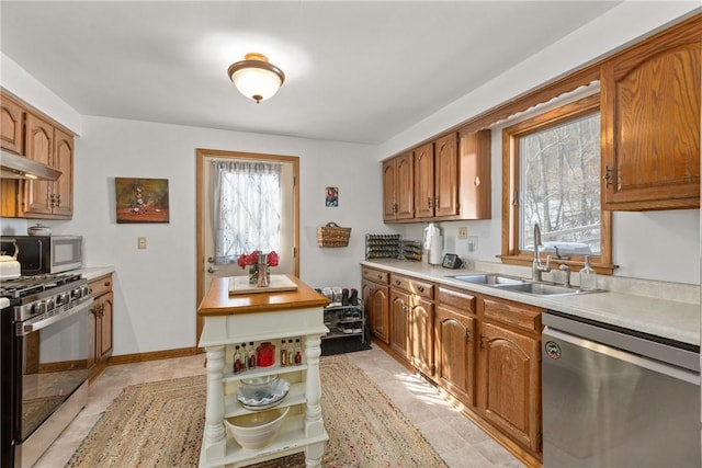 kitchen with light countertops, appliances with stainless steel finishes, brown cabinetry, and a sink