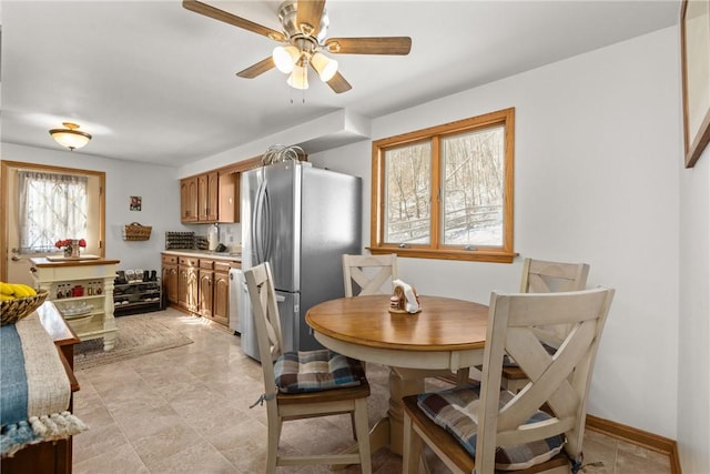 kitchen featuring ceiling fan, baseboards, light countertops, freestanding refrigerator, and brown cabinets