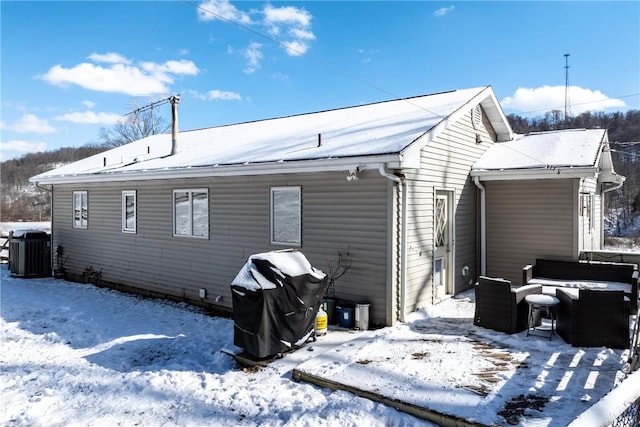 snow covered rear of property featuring central AC