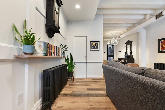 living room featuring light wood-type flooring, an inviting chandelier, radiator heating unit, and visible vents