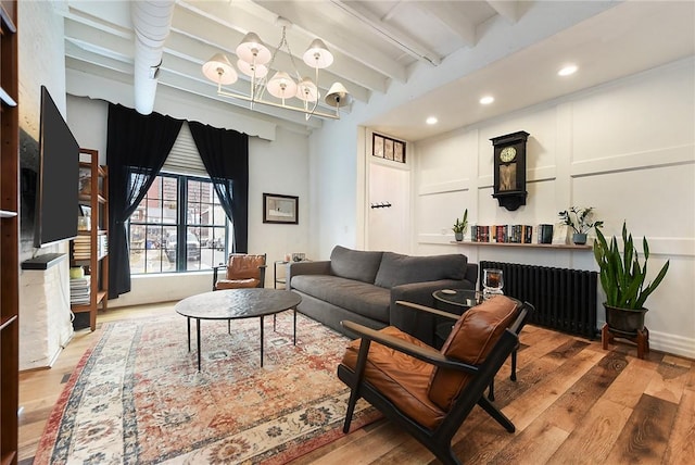 living room with beamed ceiling, an inviting chandelier, wood finished floors, and a decorative wall