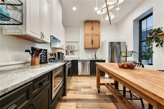 kitchen with light stone counters, pendant lighting, stainless steel appliances, light wood-type flooring, and under cabinet range hood