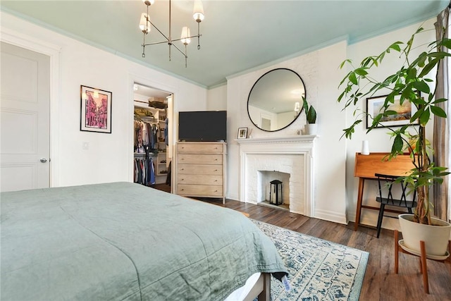 bedroom featuring an inviting chandelier, ornamental molding, a walk in closet, and wood finished floors