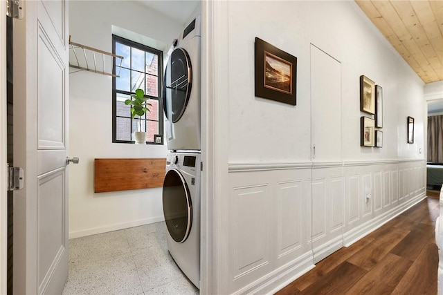 washroom with wood ceiling, stacked washer and dryer, baseboards, and laundry area