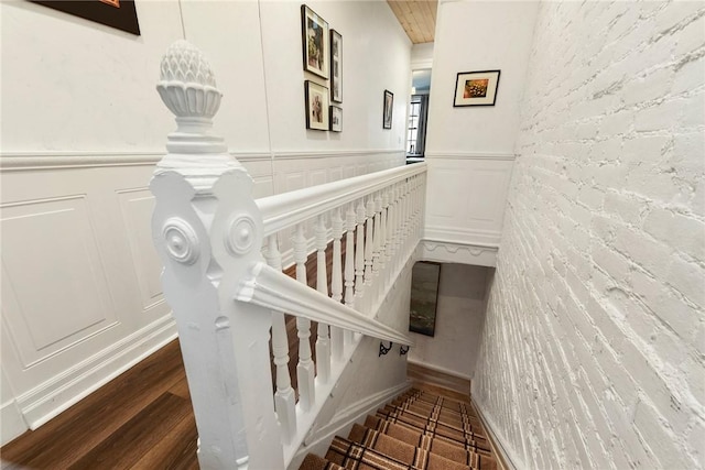 stairway featuring a wainscoted wall, brick wall, a decorative wall, and wood finished floors