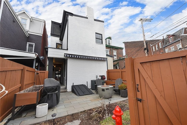 back of house with brick siding, a patio, an outdoor fire pit, a gate, and a fenced backyard