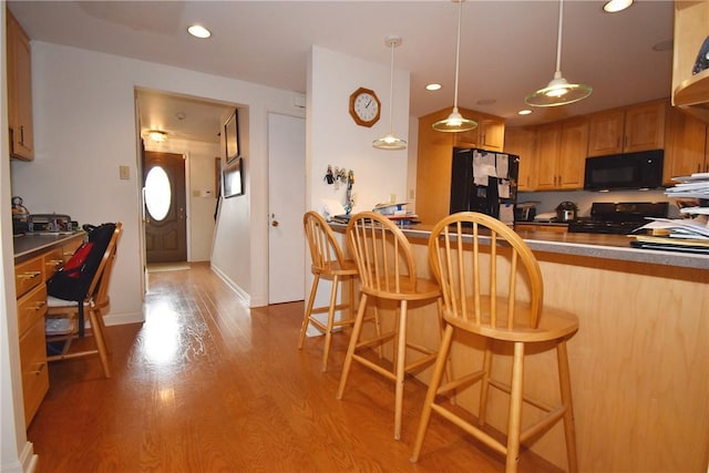 kitchen with a kitchen breakfast bar, recessed lighting, black appliances, and wood finished floors