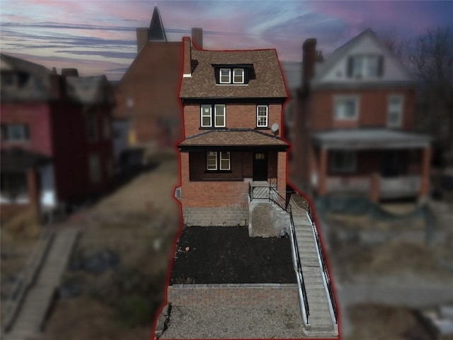 view of front of house with covered porch, brick siding, and roof with shingles