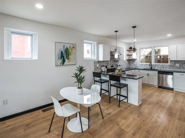 kitchen featuring stainless steel appliances, a peninsula, a sink, decorative backsplash, and dark countertops