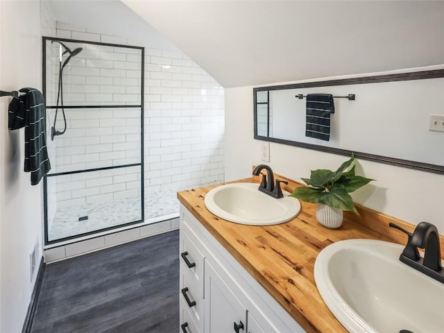 bathroom with lofted ceiling, a sink, a tile shower, and wood finished floors