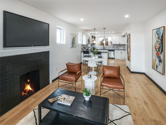 living room with light wood-style floors, recessed lighting, baseboards, and a tiled fireplace