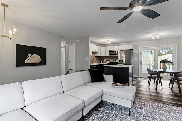 living room with ceiling fan with notable chandelier and dark wood-type flooring