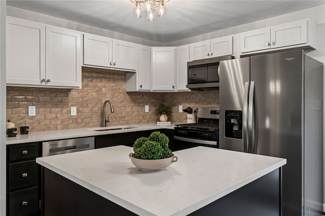 kitchen with stainless steel appliances, a kitchen island, a sink, white cabinets, and backsplash