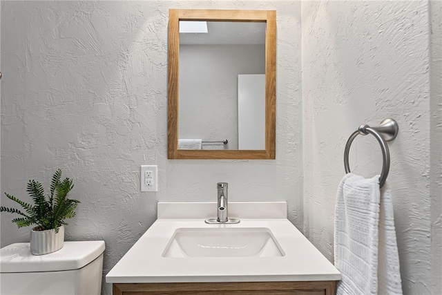 half bathroom featuring a textured wall, vanity, and toilet