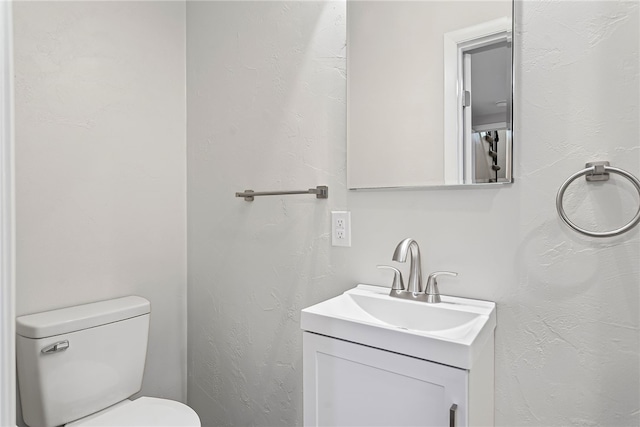 bathroom featuring a textured wall, vanity, and toilet