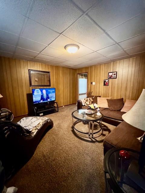 living area featuring wood walls, carpet, and a drop ceiling