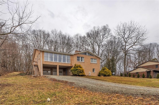 view of front of home featuring brick siding, a chimney, stairway, a garage, and driveway