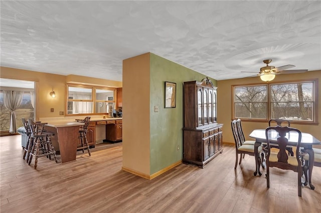 dining area featuring a ceiling fan, baseboards, a healthy amount of sunlight, and light wood finished floors